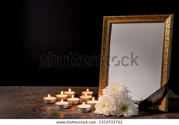 Blank funeral frame, candles and flowers on\
table against black\
background