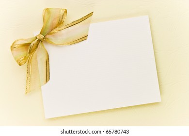 Blank Gift Tag Tied With A Bow Of Gold Satin Ribbon On Paper. Natural Texture