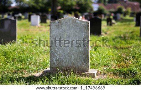 Blank gravestone with other graves and trees in background. Old stone.