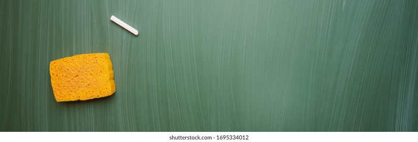 Blank green chalkboard with sponge and chalk, blackboard texture, banner size, panorama, with copyspace for your individual text. 