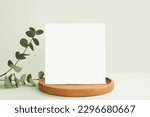 Blank Greeting Card, Invitation Mockup. Front view Eucalyptus Plant, Modern Wooden Plate, Boho Paper Mock Up on Green Table Copy Space. Minimal Business Brand Template. Soft Shadow Nordic Flier Design