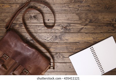 A Blank Journal Or Sketch Book And Brown Leather School Satchel On A Rustic Wooden Desk Top Background Forming A Page Border
