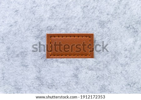 Blank label made of brown genuine leather tag sewn on to light gray felt material. Copy cpase, blank.