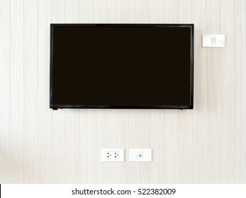 Blank Lcd Flat Screen Television Hanging At The Planks Wooden Wall With Copy Space In Living Room Or Bedroom. White Home Electrical Switch And Plug Outlet On A Light Brown Or Beige Color Wooden Wall.