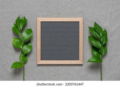 Blank Letter Board With Green Leaves, Gray Textile Background. Top View, Flat Lay.