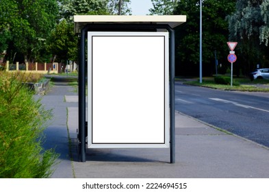 blank lightbox and glass bus shelter at busstop. green street setting. urban background. white ad poster and commercial space. display panel. empty vertical outdoor communication space. mockup base