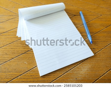 Blank lined notepad and blue pen on a wooden desk.  Perfect for concepts of writing, planning, education, or backtoschool.