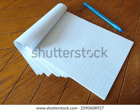 Blank lined notepad and blue pen rest on a rich woodgrain surface.  Perfect for concepts of writing, planning, notetaking, education, or backtoschool themes.