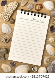 A blank lined spiral notebook surrounded by seashells, coral, and stones on a wooden surface. The summer background is suitable for text, notes, design, advertising, and travel projects.
