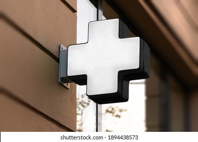 Blank Medical Cross Sign Mockup In The Urban Environment, On The Facade, Empty Space To Display Your Store Sign Or Logo