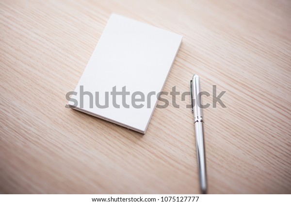 A blank memo pad and a silver pen, on a light colored\
wood table. 