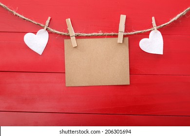 Blank message card and felt hearts with clothespins over red wooden board - Powered by Shutterstock