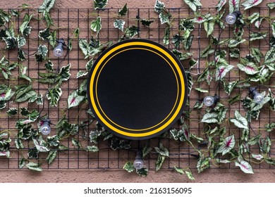 Blank Minimal Circular Shop Signboard Mockup For Design. Street Hanging Sign Board For Logo Presentation With Green Leaves Around. Cafe, Restaurant Or Bar Badge Black And Yellow Round