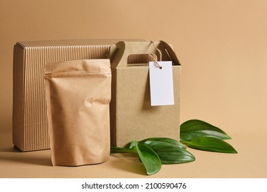 blank mockup paper bag, cardboard boxes, white tag for labeling and green fresh leaves on brown background Eco friendly packaging, paper recycling, zero waste, natural products concept. Copy space.