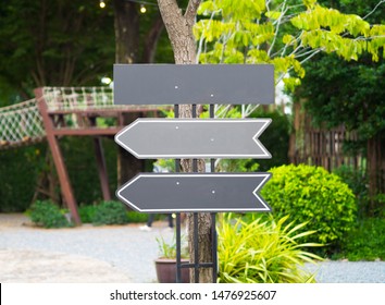 Blank modern grey signpost attached on pole pointing many directions with wooden play house, tree and bush as background. Left & Right empty copy space arrow sign for guide in park garden playground.