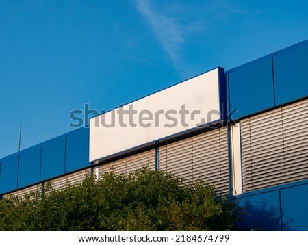 Blank name board on a building exterior. Empty white space for a company logo on a wall. Template of a signboard on an office house. Blue facade with closed window blinds. Blue sky in the background.