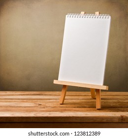 Blank Note Book On Easel On Wooden Table Over Grunge Background