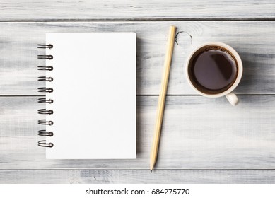 Blank note pad and coffee cup on white wooden table