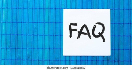 blank note pad with FAQ text on green wooden blue background