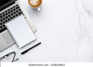 Leeres Notebook ist auf Laptop-PC mit Schreibtisch aus weißem Marmor mit einer Tasse Latte-Kaffee und Bürobedarf. Draufsicht mit Kopienraum, flach gelegt.
