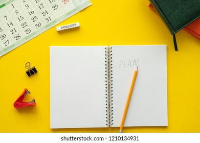 Blank notebook page is on top of yellow office desk table. on the table is a calendar, diaries, a notebook with a pencil and a plan inscription. Top view, flat lay. - Powered by Shutterstock