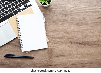 Blank notebook with pen are on top of wood office desk table with laptop computer, and supplies. Top view with copy space, flat lay. - Shutterstock ID 1715448142