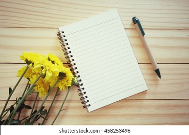blank notebook with pen and yellow bouquet of flowers  wooden table.diary writing concept

