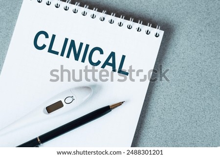 Blank notebook with thermometre and pen on table. CLINICAL text.