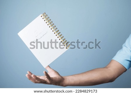 Blank notepad hovering over businessman's hand on light blue background, copy space for your text