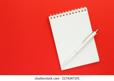 Blank notepad on spirals and pen on bright red background. Sketchbook for drawing or notes. Art and hobby concept. Top view, flay lay with copy space.
