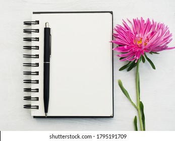 Blank notepad page and a beautiful flower. Close-up, view from above, wooden surface. Concept of preparation for a professional holiday. Congratulations for relatives, friends and colleagues