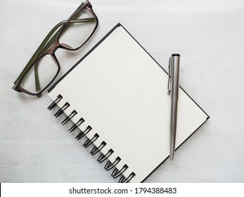 Blank notepad page, pen and glasses. Greeting card. Close-up, view from above, wooden surface. Concept of preparation for a professional holiday. Congratulations for relatives, friends and colleagues