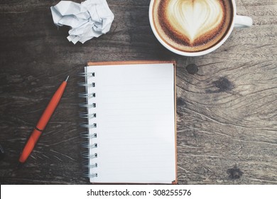Blank notepad and pen with latte art coffee on office table