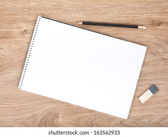 Blank notepad, pencil and eraser on the wooden table. View from above