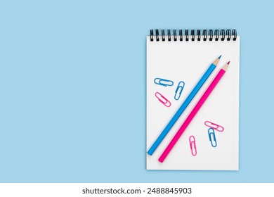 Blank notepad, pencils and paper clips on a blue background. Back to school. Teacher's Day. Top view. Flatlay composition. Copy space.