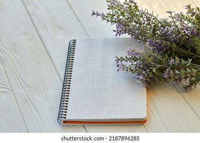 Blank Notepad And Purple Flowers On Wooden Desk. Checkered Page For Copy Space.