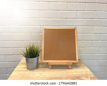 Blank Noticeboard With Plant Pot On Wooden Table And White Brickwall