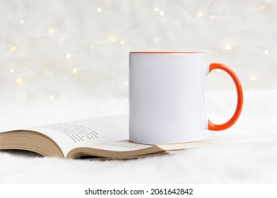 Blank Orange Handle Mug On The Book  With White Bokeh Lights. 11 Oz White Ceramic Mug Mock Up Photo.