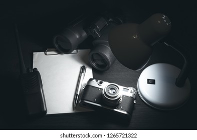 Blank Page With Copy Space, Pen, Portable Radio, Binoculars And Photo Camera On A Black Spy Agent Table Background. Top Secret Documents. Detective Agent Dossier. Interrogation Report.