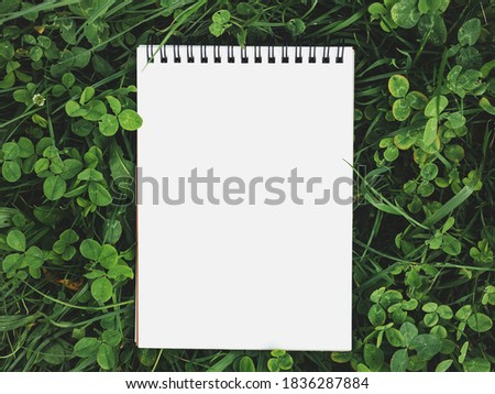 Blank page of the Notebook lying on a bright clover. View from above, close-up