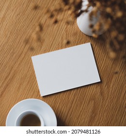 Blank paper card mockup on wooden table with cup of coffee and vase of dry flowers. Flat lay, top view. - Powered by Shutterstock