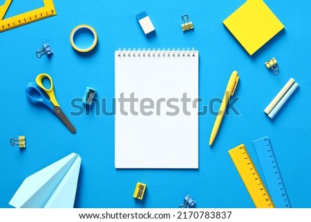 Blank paper notepad mockup with school supplies on blue background. Flat lay, top view, copy space. Back to school concept. Blue and yellow office stationery.