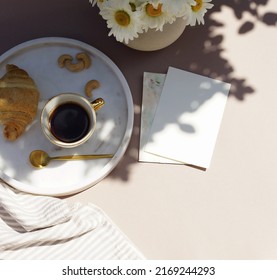 Blank paper sheet card mockup in  breakfast still life scene.Cup of coffee, croissant , daisy flowers in a vase top view on beige desk with sunlight shadows. Feminine lifestyle composition.  - Shutterstock ID 2169244293