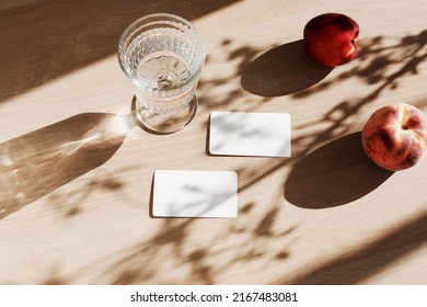 Blank paper sheet cards mockup, glass water, fruits and floral shadow top view on beige wooden background. Summer stationary template.Copy space. Flat lay minimal business brand template .Card mock up