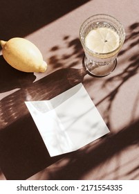 Blank Paper Sheet Cards Mockup,lemon,lemonade Glass And Floral Shadow Top View On Brown   Background. Copy Space. Flat Lay   Minimal Business Brand Template Neutral Color. Card Mock Up.