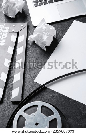 Blank paper sheet with movie clapper and film reel on dark background, closeup