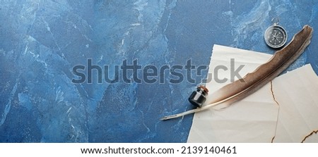 Blank paper sheets, quill, ink and compass on blue grunge background with space for text