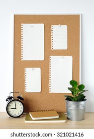 Blank Papers On Cork Board, Notebooks, Alarm Clock And Tree On Wood Table Over White Cement Wall Background, Template