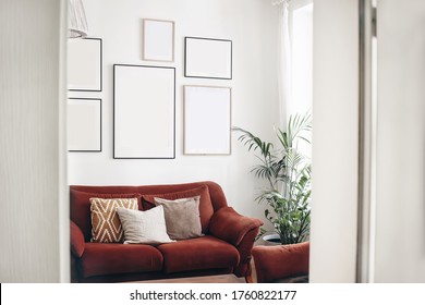 Blank picture frames mockups on white wall. White living room design. View of  modern boho, scandi style interior with sofa, cushions, potted palm plant through open white door. Home staging concept.