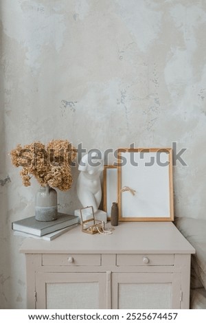 Blank picture frames next to a white statue, a vase with dried flowers and books along with assorted accessories on a dresser in the bedroom